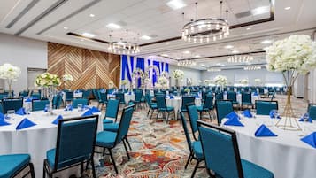 A banquet hall with round tables, blue chairs, and floral centerpieces.