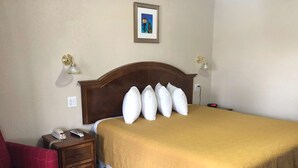 A hotel room with a large bed, a wooden nightstand with a phone, a red chair, and a framed picture on the wall.