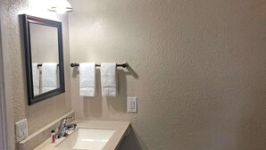 A bathroom with a white sink, a mirror, and two white towels hanging on a towel bar.
