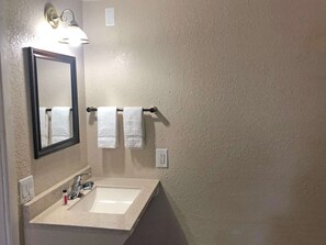 A bathroom with a white sink, a mirror, and two white towels hanging on a towel bar.