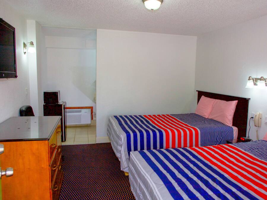 A hotel room with two beds, a desk, a chair, a television, and a telephone.