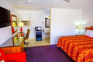 Una habitación de hotel con una cama, un escritorio con silla, un espejo y un televisor.