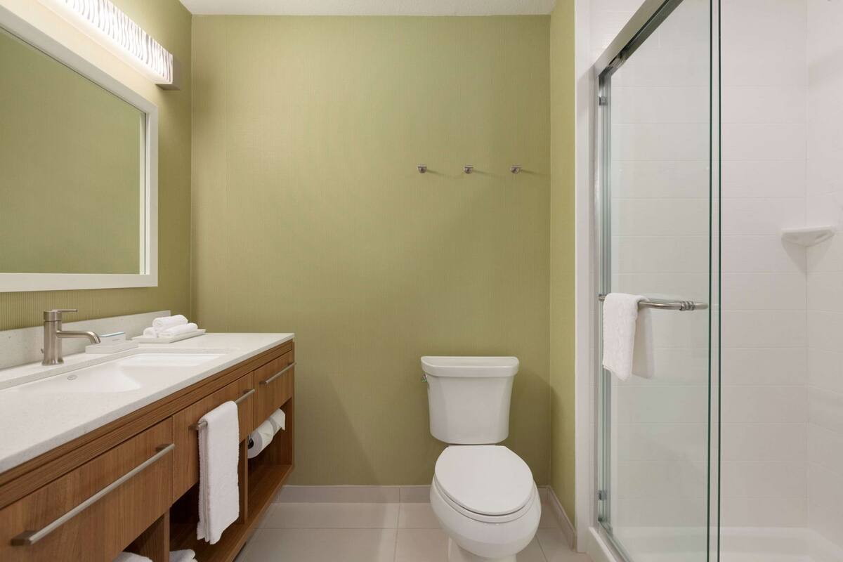 A bathroom with a wooden vanity, a toilet, and a glass shower enclosure.