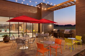 An outdoor patio with tables and chairs, a barbecue grill, and string lights. - Home2 Suites by Hilton Oklahoma City Quail Springs (Oklahoma City)