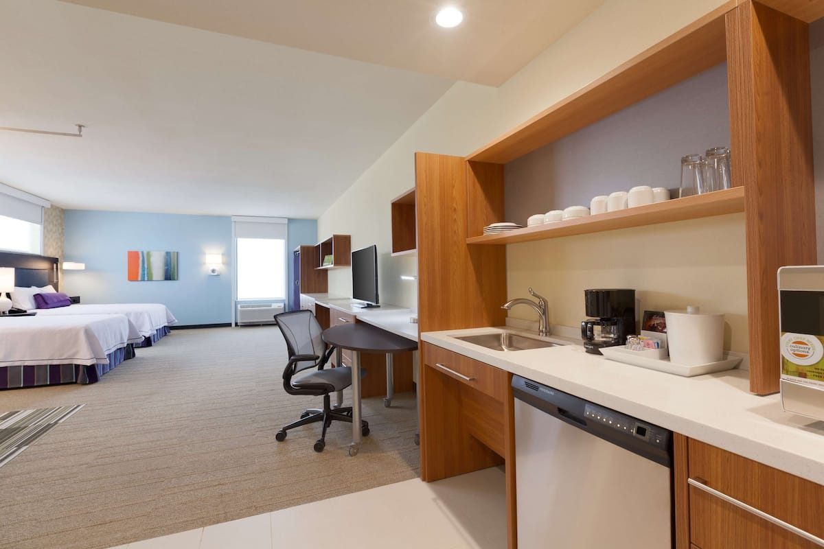 A modern hotel room with a kitchenette, a bed, a desk, and a chair.