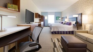 Une chambre d’hôtel équipée d’un bureau, d’une chaise, d’une télévision, de deux lits, d’un canapé et d’une grande fenêtre.