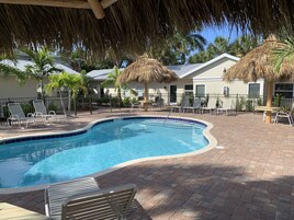 A swimming pool with lounge chairs and a thatched roof structure.