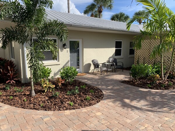 A house with a patio area featuring a brick walkway, outdoor furniture, and various plants. - Twin Palms at Siesta (Siesta Key)