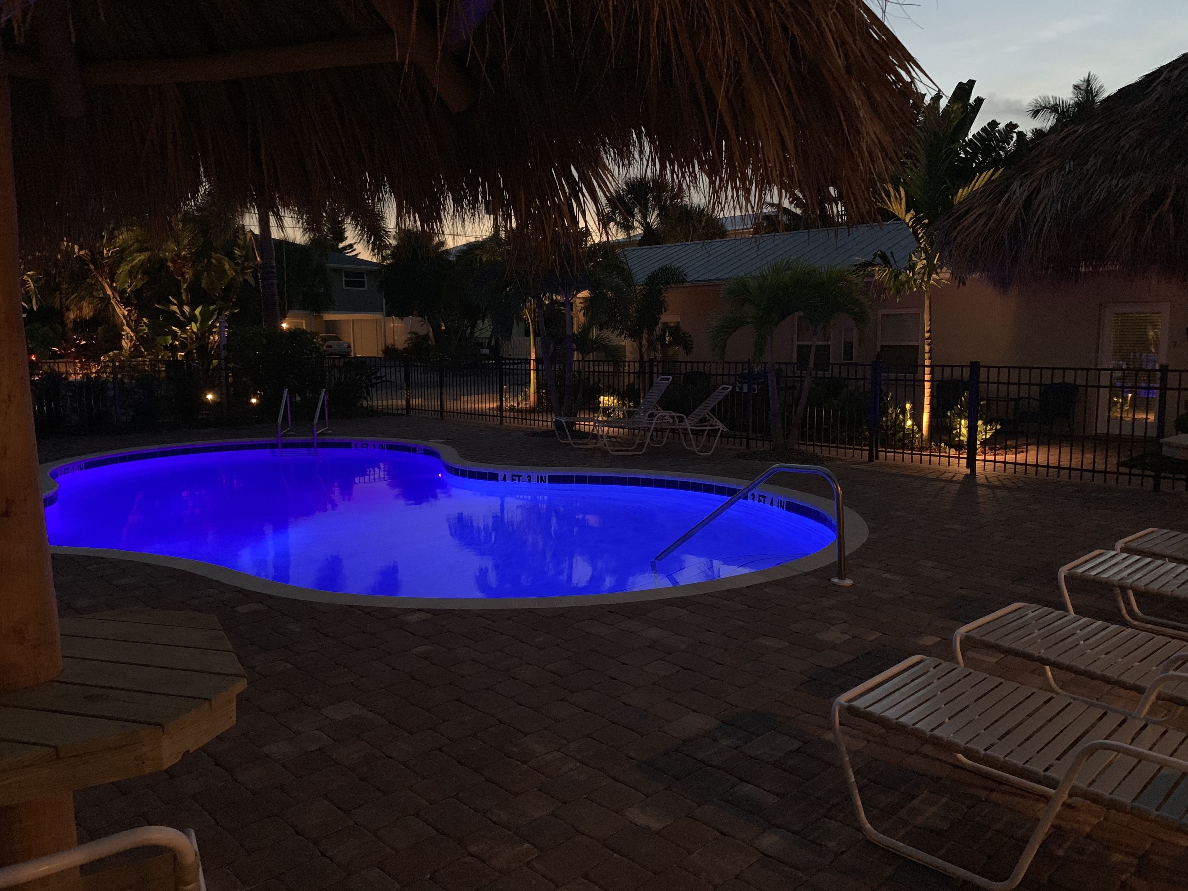 A swimming pool with a blue tint, surrounded by lounge chairs and a brick patio.
