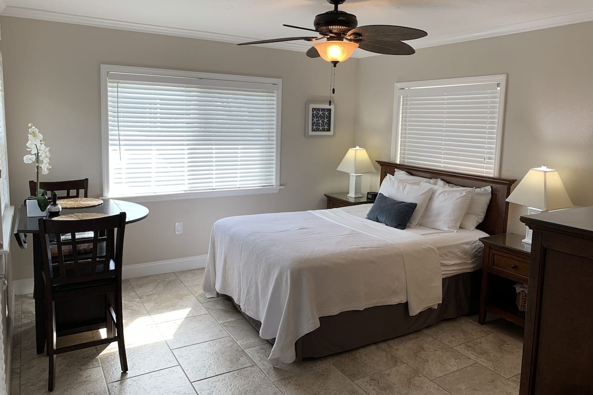 A bedroom with a bed, two bedside tables with lamps, a ceiling fan, and a window with blinds.