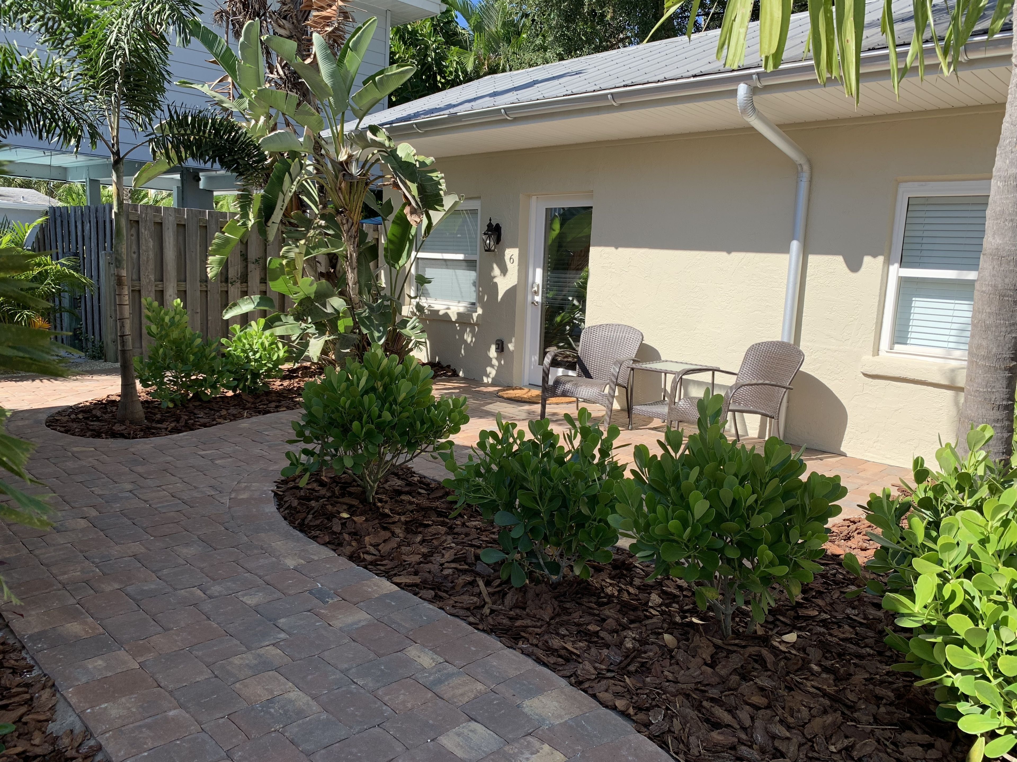 Eine Terrasse mit gepflastertem Weg, Gartenmöbeln und verschiedenen Pflanzen.