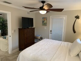 Un dormitorio con cama, cómoda, televisor, ventilador de techo, una puerta y decoración en la pared.