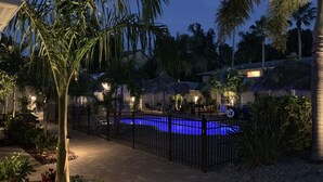 Ein nächtlicher Blick auf einen Swimmingpool, umgeben von Palmen und einem Ziegelweg.