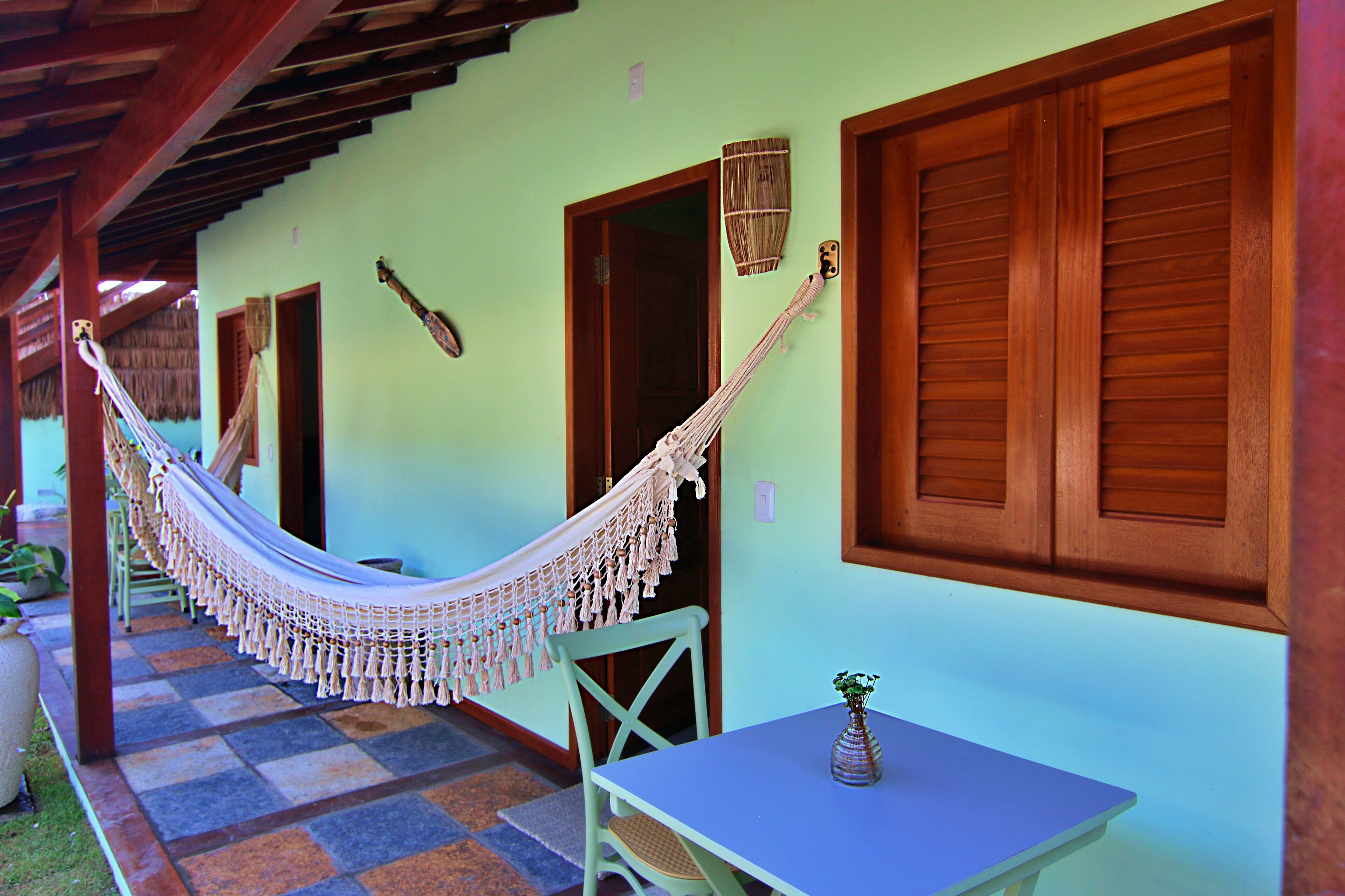 A hammock, a table, and a chair in a covered outdoor area with a checkered floor.