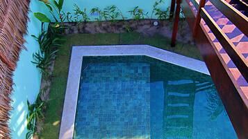 A swimming pool with a tiled edge, surrounded by a grassy area and a wooden deck.