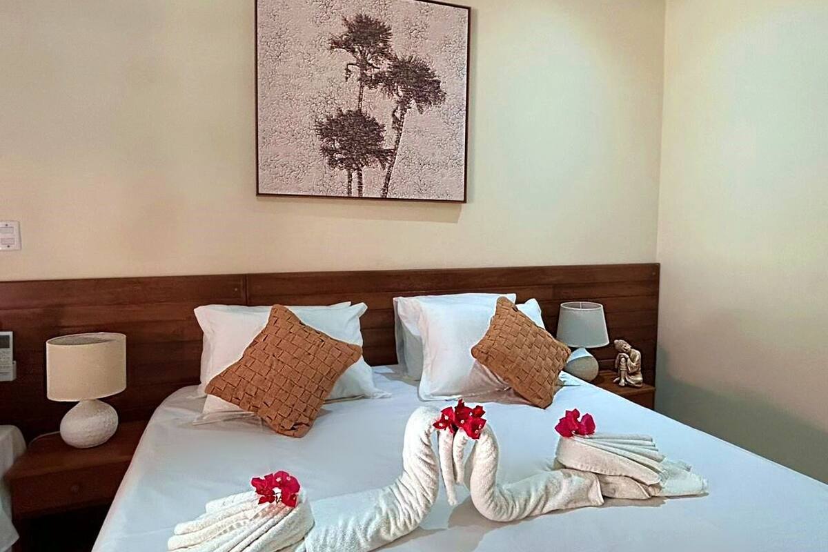 A hotel room with a neatly made bed, pillows, and a wall-mounted artwork.