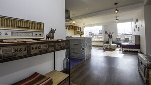 A modern living room with a vintage radio, a cat statue, and a city view through large windows. - Terra Nostra Suites (Cusco)