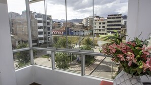 A room with a large window overlooking a cityscape, a vase with flowers, and a wooden floor. - Terra Nostra Suites (Cusco)