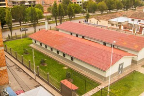 A two-story building with a red-tiled roof, surrounded by a green lawn and a fence. - Terra Nostra Suites (Cusco)