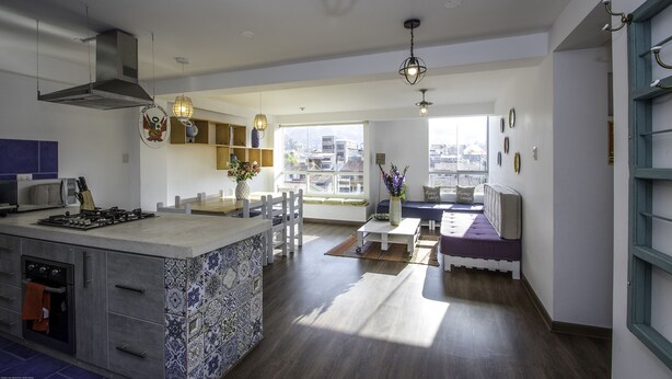 A modern kitchen with a central island, built-in oven, and a dining area with a bench and table. - Terra Nostra Suites (Cusco)