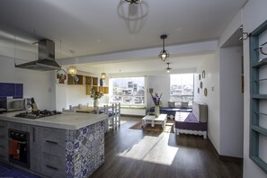 A modern kitchen with a central island, built-in oven, and a dining area with a bench and table. - Terra Nostra Suites (Cusco)