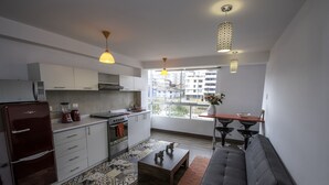 A modern kitchen with white cabinets, a refrigerator, and a dining area with a sofa and table. - Terra Nostra Suites (Cusco)