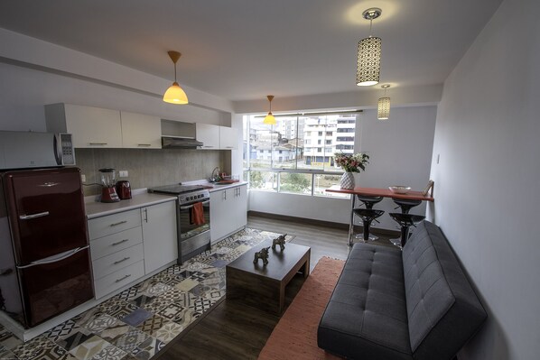 A modern kitchen with white cabinets, a refrigerator, and a dining area with a sofa and table.