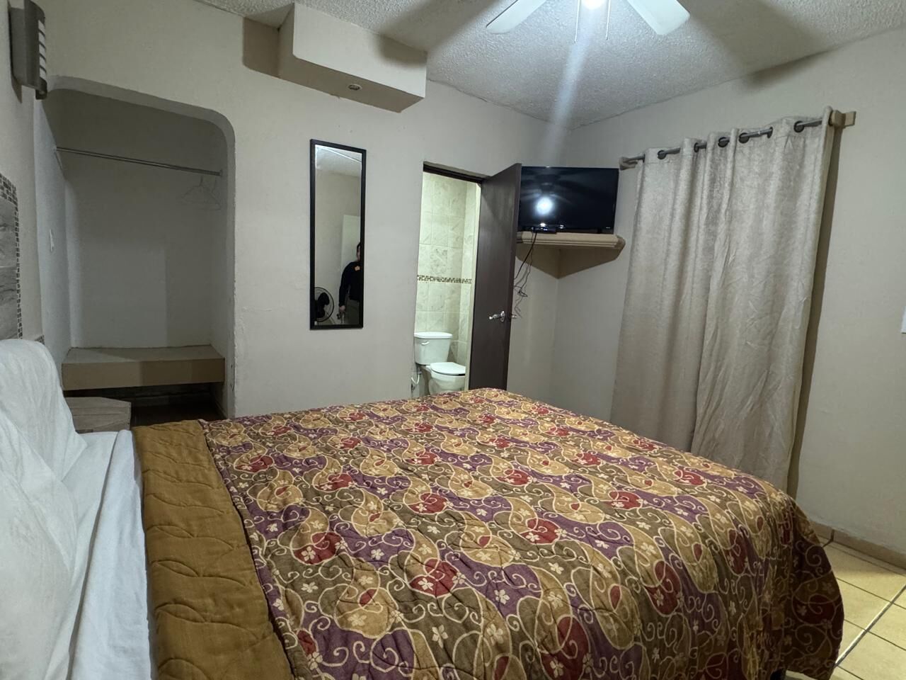 Quarto com cama, armário, televisão e banheiro visível por uma porta aberta.
