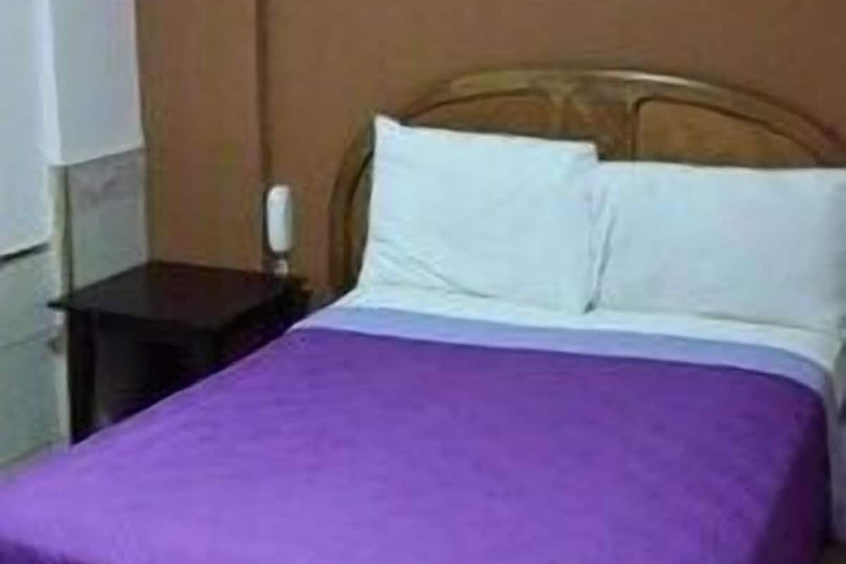 Une chambre d’hôtel standard, équipée d’un lit, d’une table de chevet et d’une lampe fixée au mur.