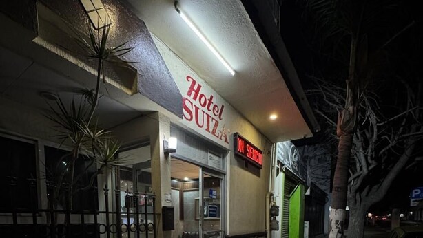 A hotel entrance with a sign reading "Hotel Suiza" and a digital display indicating "No Vacancy".