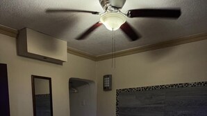 A bedroom with a bed, a ceiling fan, a mirror, and a wall-mounted light fixture.