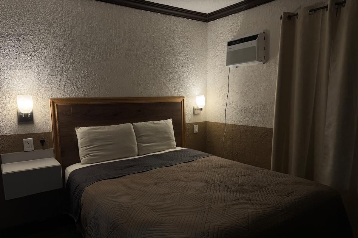 Une chambre d’hôtel équipée d’un lit, de lampes de chevet, d’une table de nuit et d’un climatiseur fixé au mur.