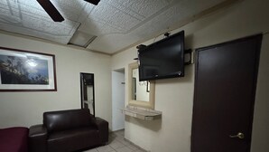 A room with a brown leather sofa, a flat-screen TV mounted on the wall, a framed picture, and a door.