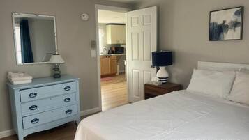Une chambre à coucher avec un lit, une commode, un miroir, une porte et un tableau accroché au mur.
