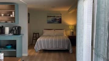 Een slaapkamer met een bed, een bureau en een stoel. Er is een raam met gordijnen en een schilderij aan de muur.