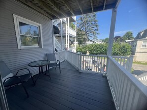 A covered porch with a table and chairs, a white railing, and a view of the neighborhood.