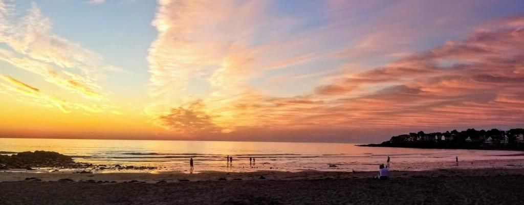 A beach scene with a sunset, calm sea, and distant shoreline.