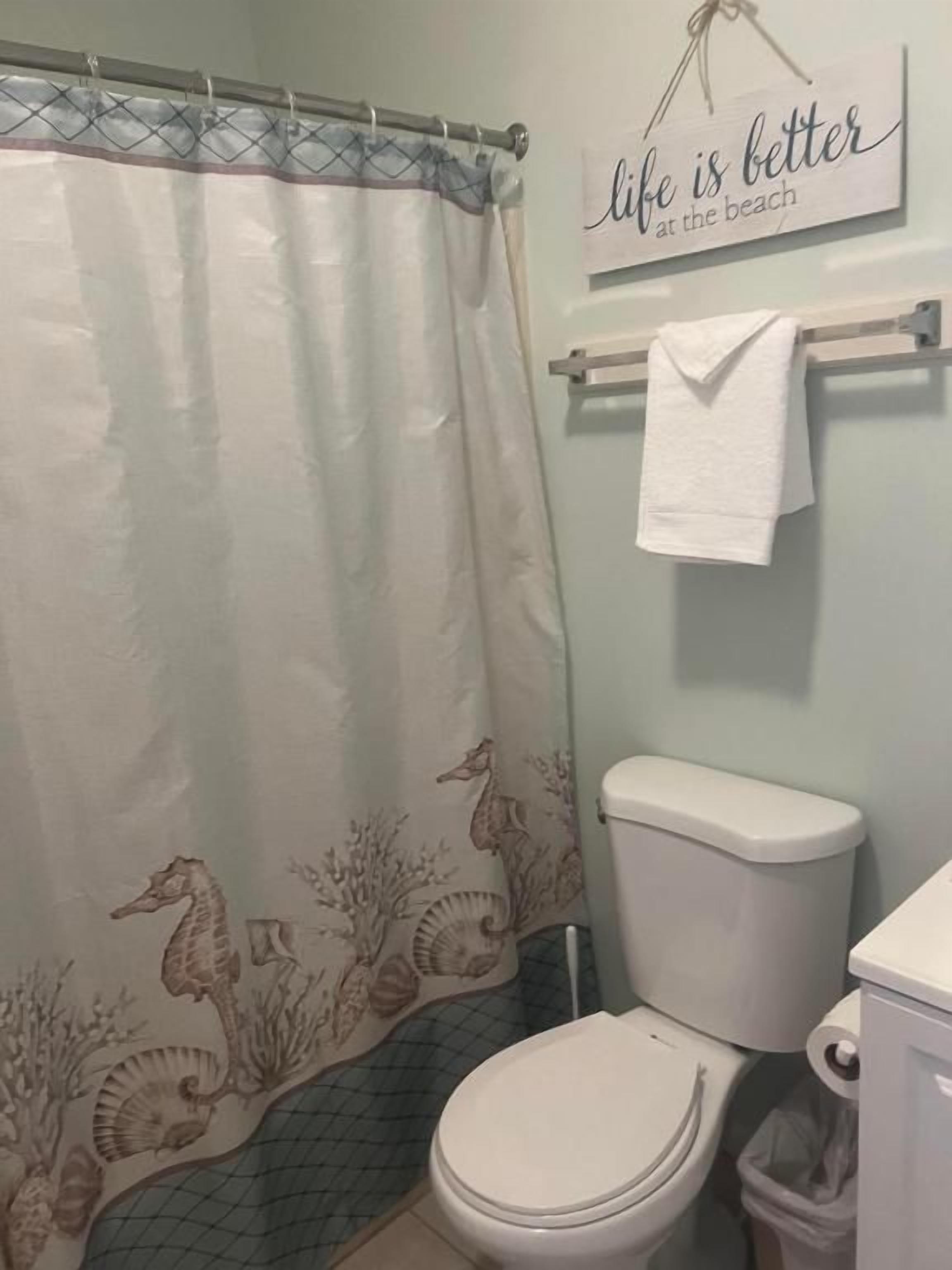 A bathroom with a toilet, a shower curtain with a seahorse pattern, and a towel rack with a towel.