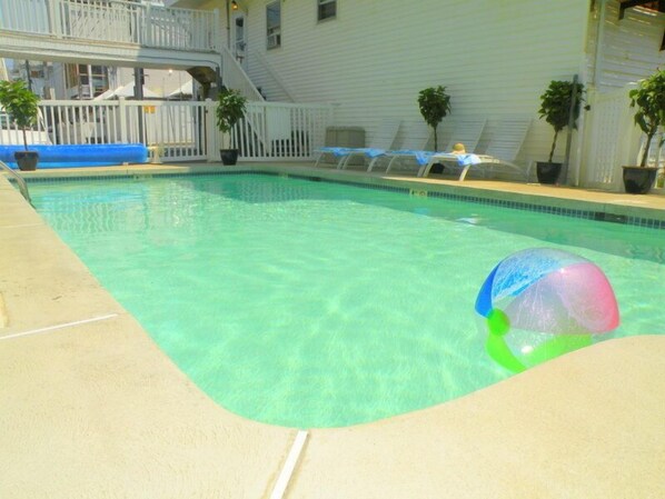 A swimming pool with clear water, a lounge area with umbrellas, and a white building with a balcony in the background. - The Pelham Resort Motel (Hampton)
