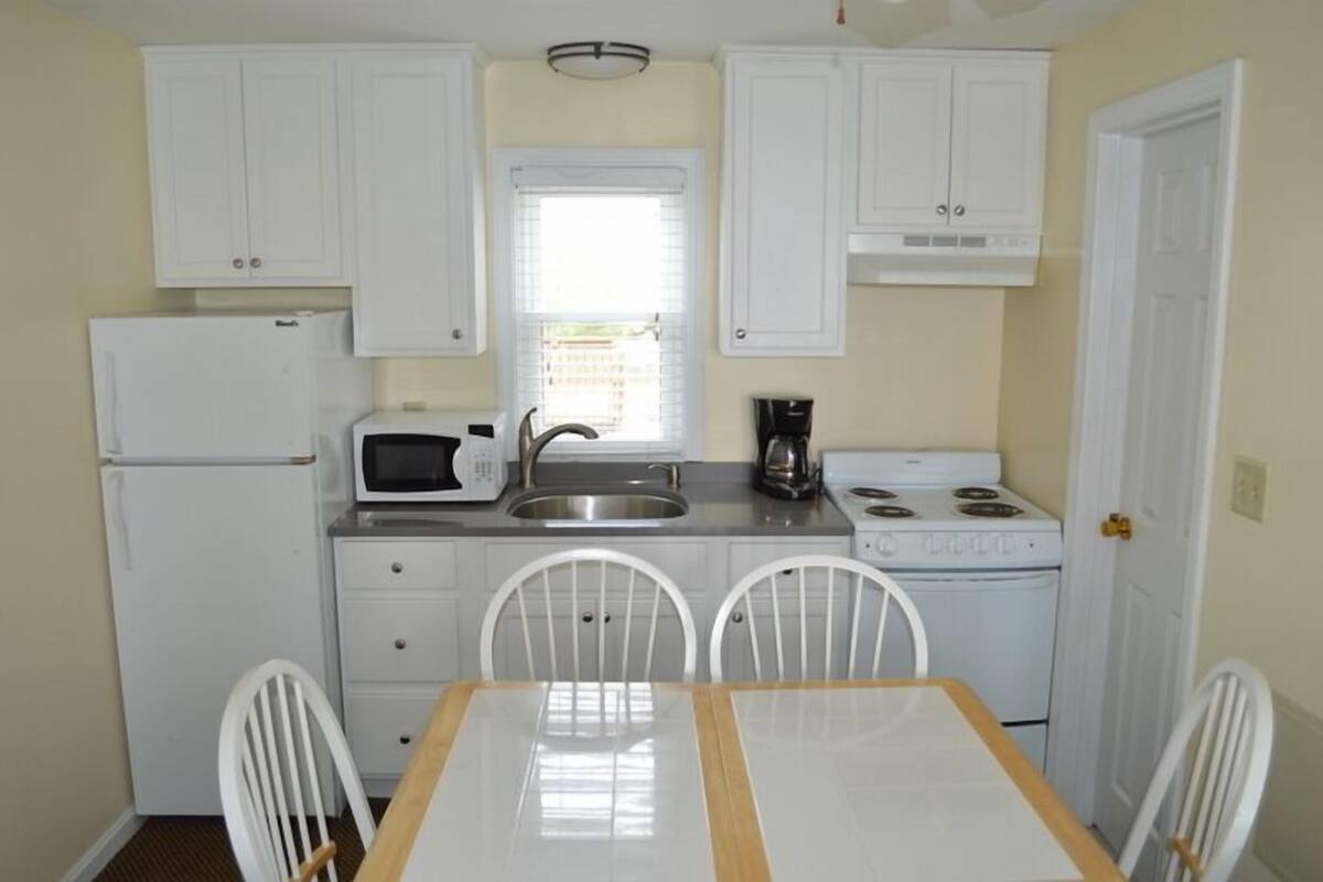 A compact kitchen with white cabinets, a microwave, a sink, a stove, and a dining table with chairs.