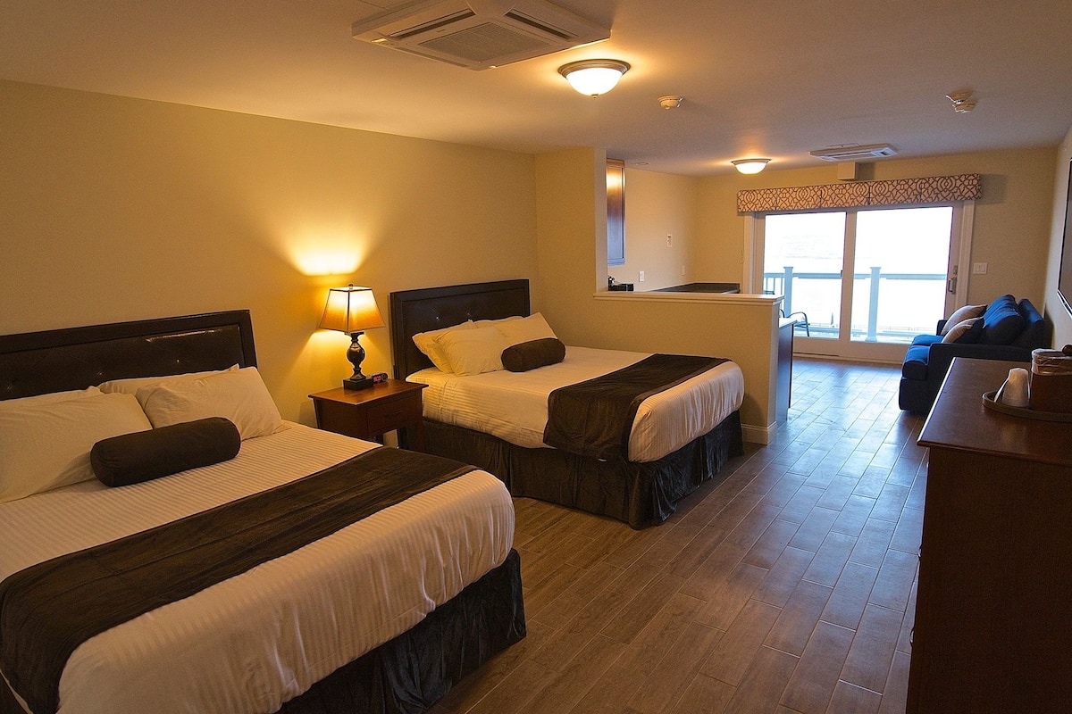 A hotel room with two beds, a desk, and a balcony with a view.