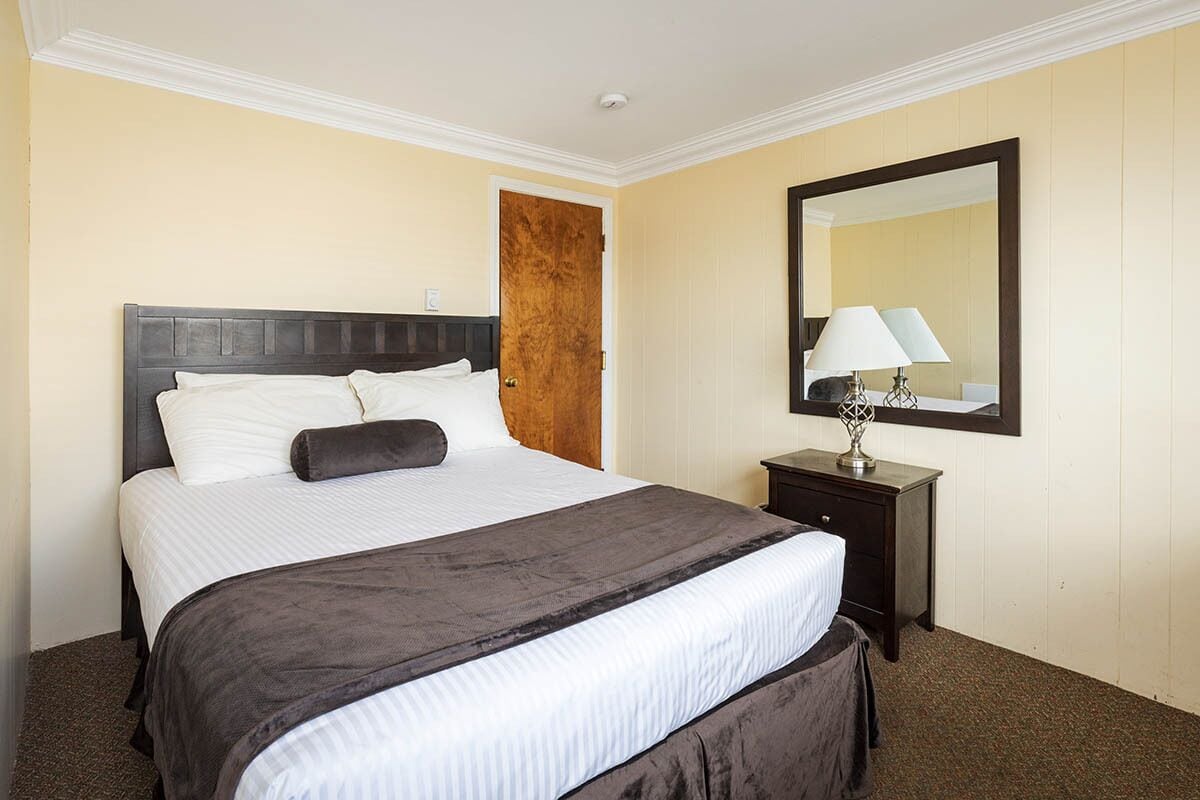 A hotel room with a large bed, a nightstand, a mirror, and a door.
