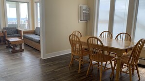 A dining area with a wooden table and chairs, a built-in air conditioning unit, and a view through large windows. - The Pelham Resort Motel (Hampton)
