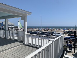 A beachside promenade with a wooden deck, a covered seating area, and a view of a crowded beach with umbrellas. - The Pelham Resort Motel (Hampton)