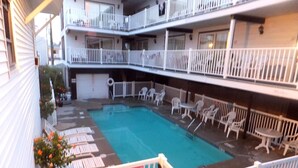 A multi-level hotel with a pool area, including a pool, lounge chairs, and a sign indicating pool rules. - The Pelham Resort Motel (Hampton)