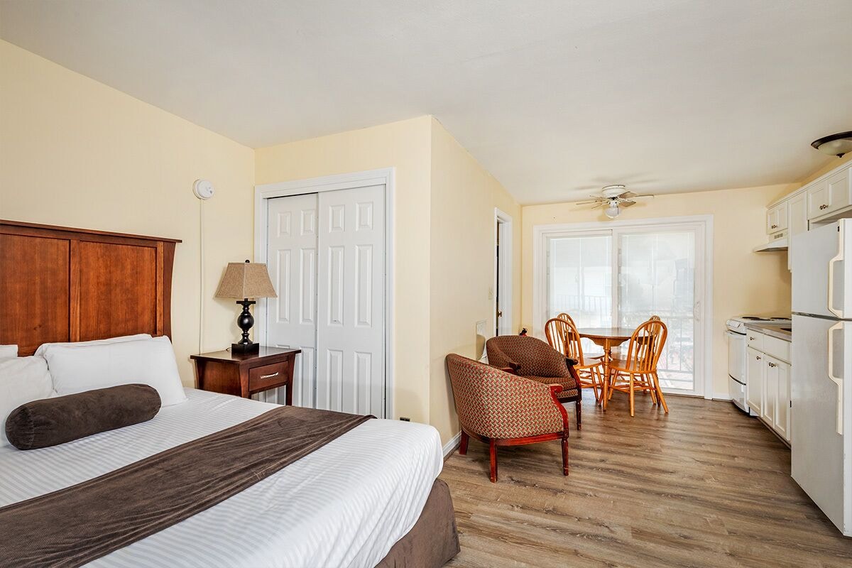 A hotel room with a bed, a desk, a chair, a dining table, and a kitchenette.