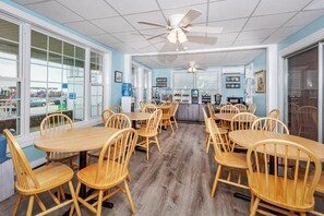 A spacious dining area with multiple wooden tables and chairs, large windows, and a ceiling fan. - The Pelham Resort Motel (Hampton)