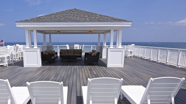 A covered outdoor seating area with white chairs and a gazebo overlooking the ocean. - The Pelham Resort Motel (Hampton)