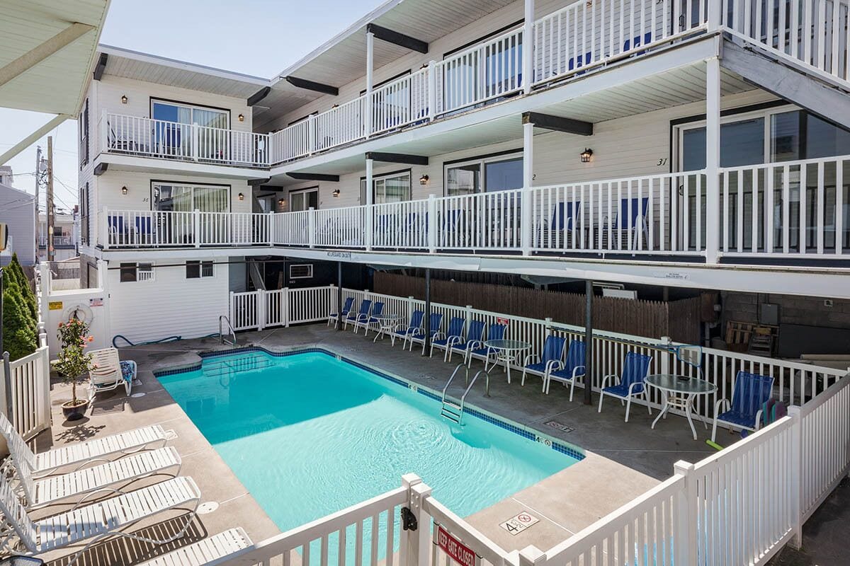 A multi-story building with a swimming pool, outdoor seating, and a fenced balcony area.