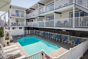 A multi-story building with a swimming pool, outdoor seating, and a fenced balcony area. - The Pelham Resort Motel (Hampton)